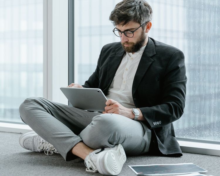 Man Sitting On Floor Pressing Tab With Paper With Price Chart On Floor